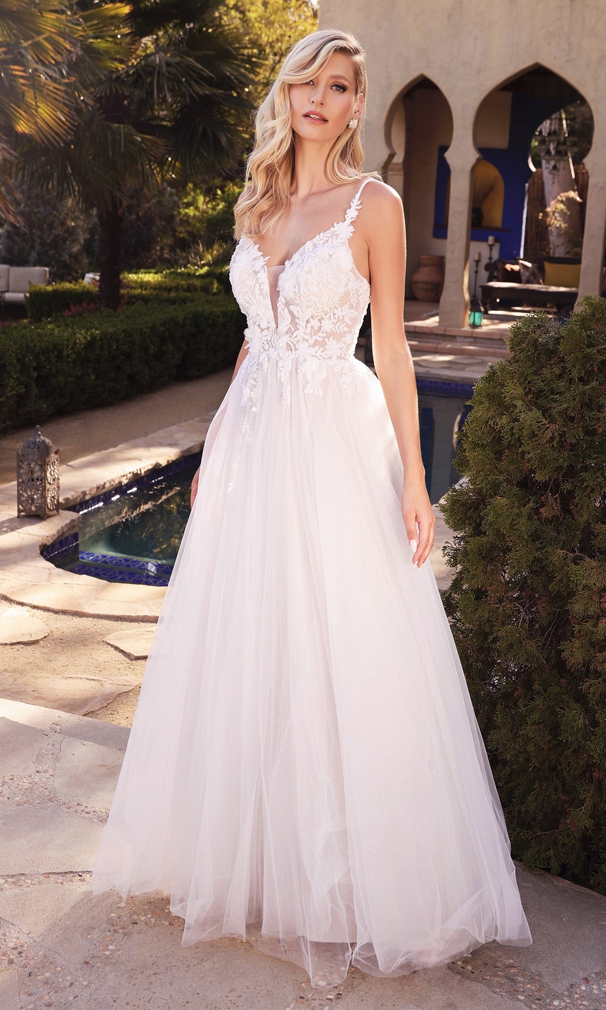 A woman stands outside wearing the Classic Off-White Long Prom Dress: Ladivine CB072W, featuring a sleeveless deep V-neck, tulle skirt, and delicate floral lace details.